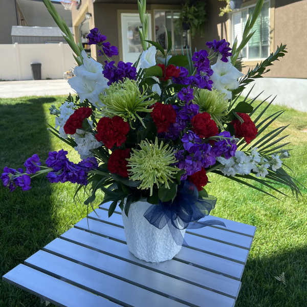 Large mixed floral arrangement in a white vase with purple, red, and white blooms