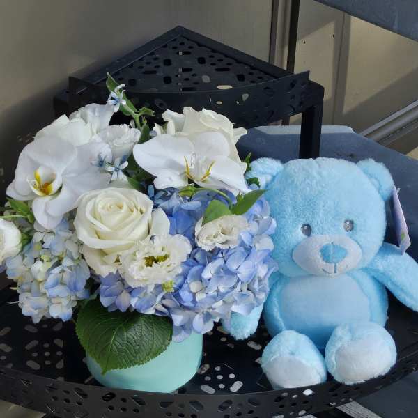 White and blue flower arrangement beside a light blue teddy bear