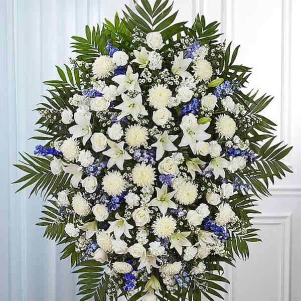 Large white and blue funeral spray with lilies, roses, and palm fronds