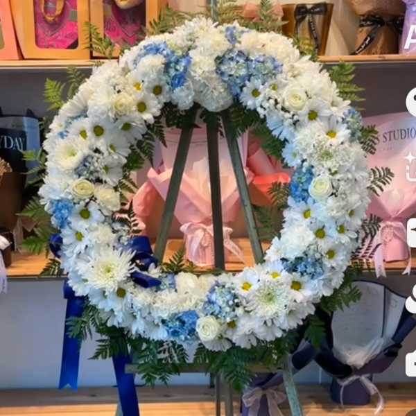 Large circular floral wreath of white and blue flowers on a stand