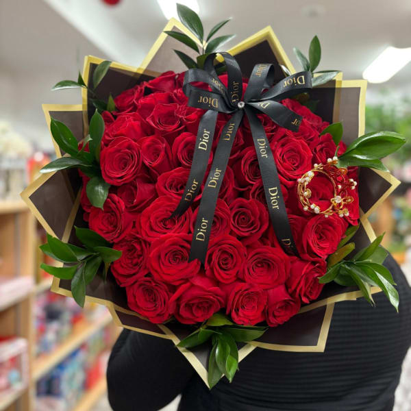 Large bouquet of red roses wrapped in black and gold paper with a Dior ribbon