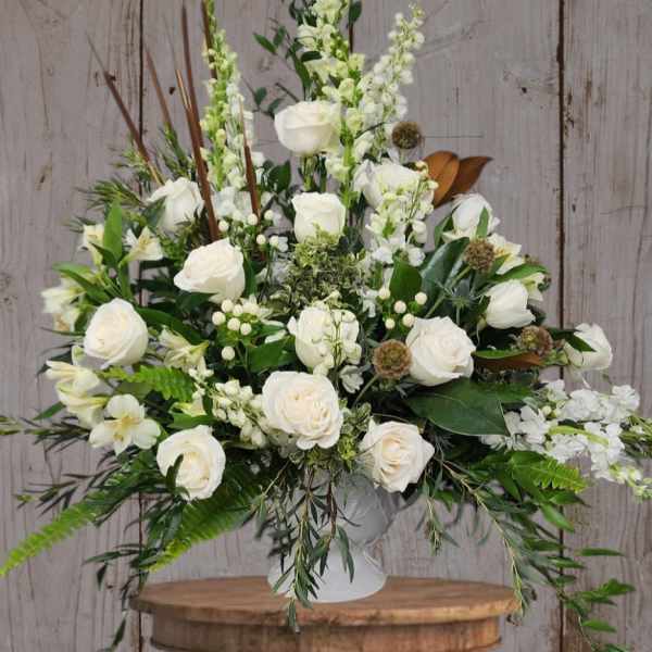 White rose arrangement in a white vase with mixed greenery