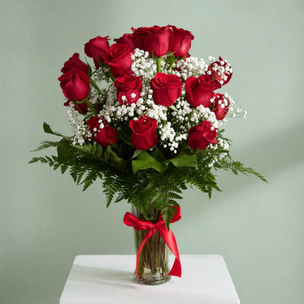 Red roses and baby's breath in a glass vase with a red ribbon