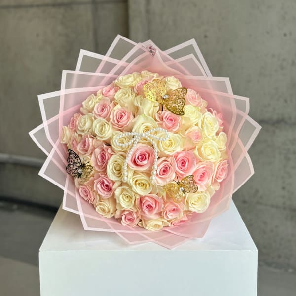 Bouquet of pink and cream roses wrapped in pink paper with butterfly accents
