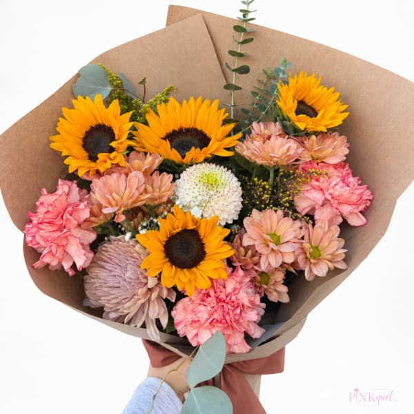 Bouquet of sunflowers, pink carnations, and pastel chrysanthemums wrapped in brown paper