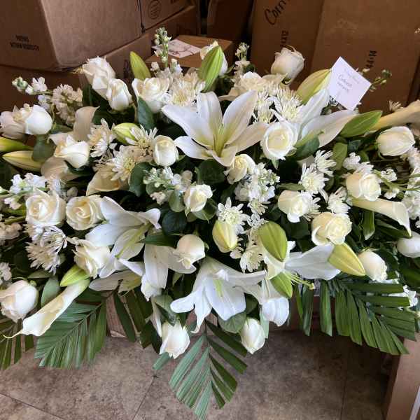 Long, low arrangement of white lilies and roses with other white blooms and large palm leaves.