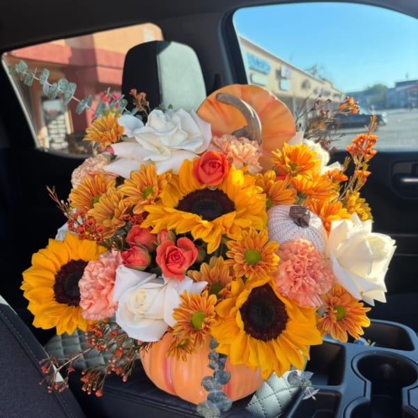 Pumpkin-shaped floral arrangement with sunflowers, roses, and carnations in a car seat