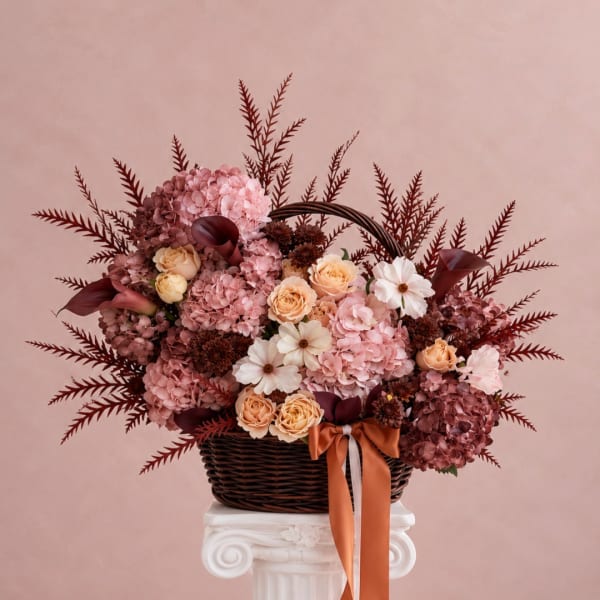Pink and peach floral arrangement in a wicker basket with ribbon