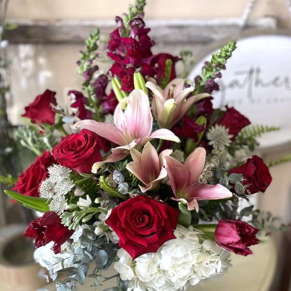Bouquet of red roses, pink lilies, and white hydrangeas in a glass vase