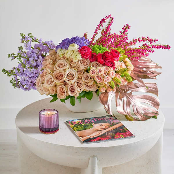 Mixed bouquet of roses and purple flowers in a white vase with a candle