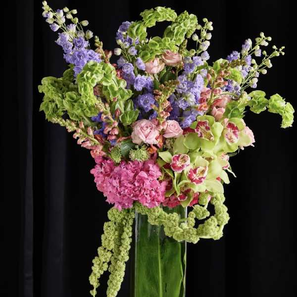 Tall mixed floral arrangement in a clear glass vase with pink, purple, and green blooms