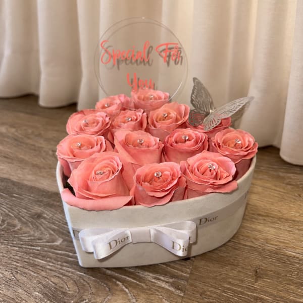 Pink roses arranged in a heart-shaped box with a clear topper