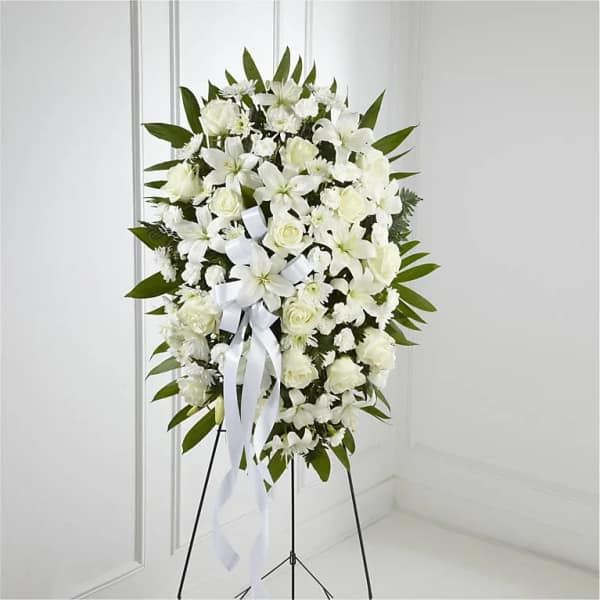 Tall standing spray of white lilies and roses with a white bow on a metal easel