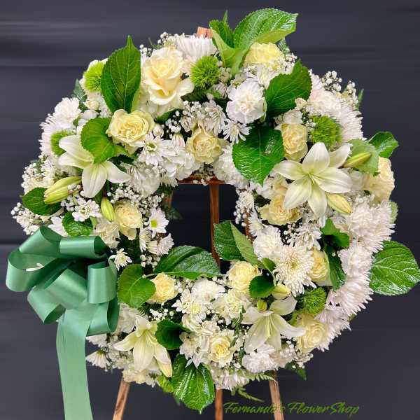 Standing wreath of white and pale yellow roses, lilies, and mums with a large green ribbon bow on an easel