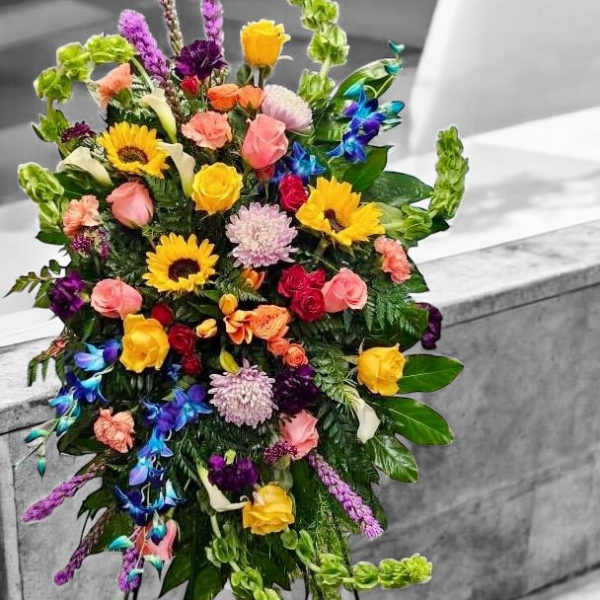 Tall multicolored standing spray with sunflowers, roses, orchids, and other blooms on a metal easel