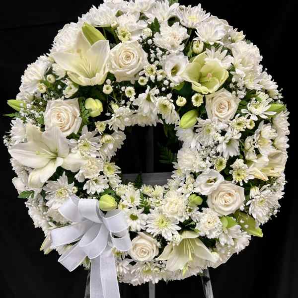 Standing white funeral wreath of roses, lilies, and chrysanthemums with a bow on a metal easel
