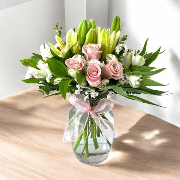 Pink roses and white lilies in a glass vase with a pink ribbon
