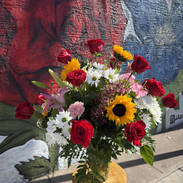 Bouquet of red roses, sunflowers, and white daisies in a glass vase