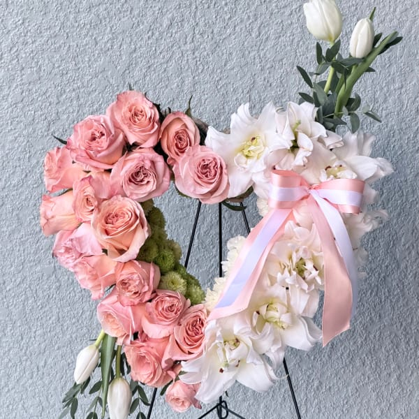 Heart-shaped floral wreath with pink roses and white orchids, tied with a pink ribbon.