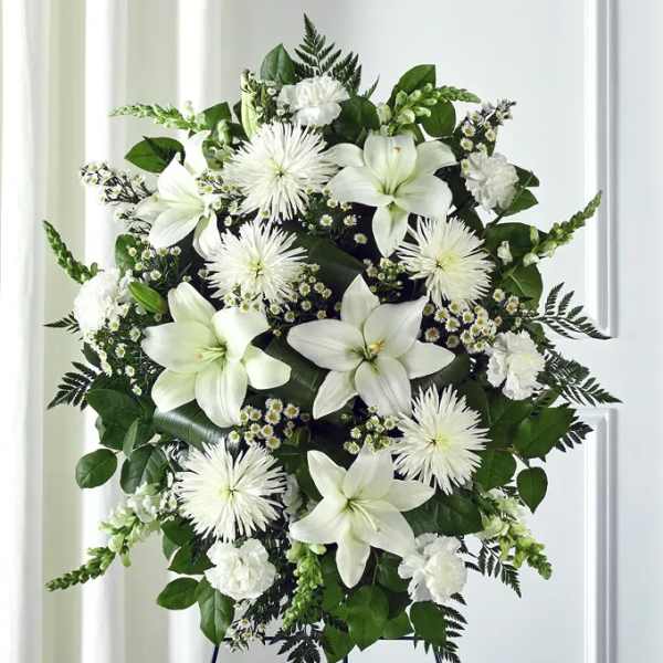 White floral standing spray on an easel with lilies and spider mums