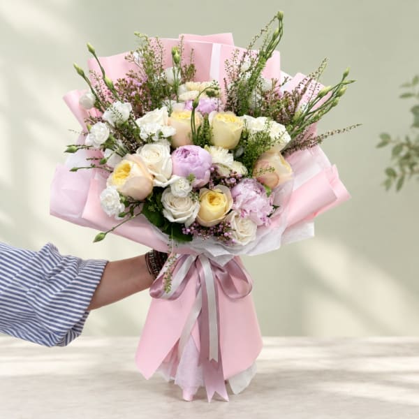 Handheld bouquet of pastel roses and lisianthus wrapped in pink paper