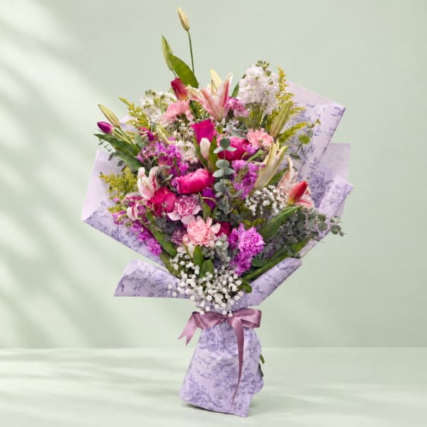 Pink and purple mixed bouquet wrapped in lavender paper with a satin ribbon