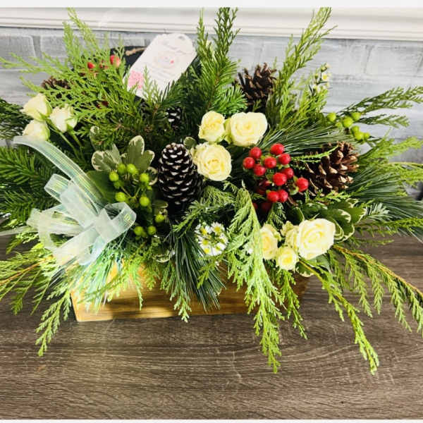 Holiday floral arrangement with cream roses, pinecones, and evergreen branches in a wooden box
