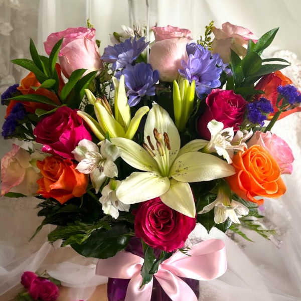 Mixed bouquet of roses and lilies in a purple vase with a pink ribbon