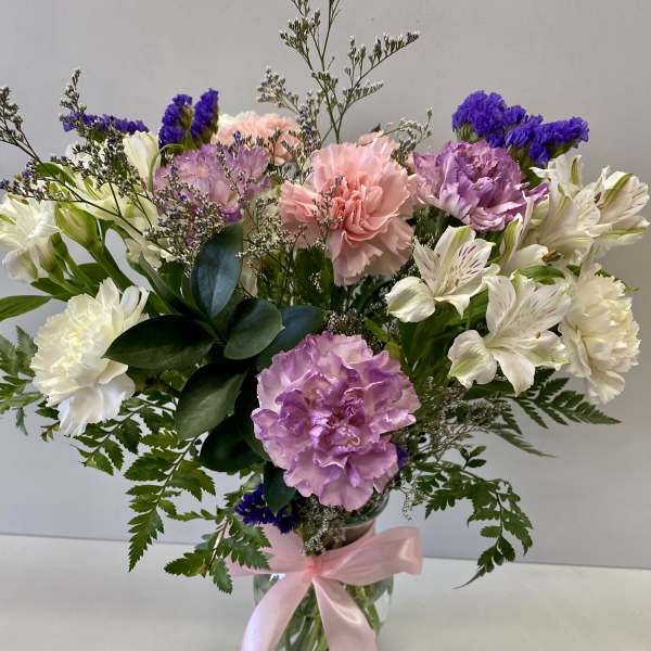 Bouquet of pink, purple, and white flowers in a glass vase with a pink ribbon