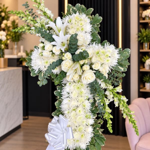 White floral cross arrangement with lilies, roses, and chrysanthemums