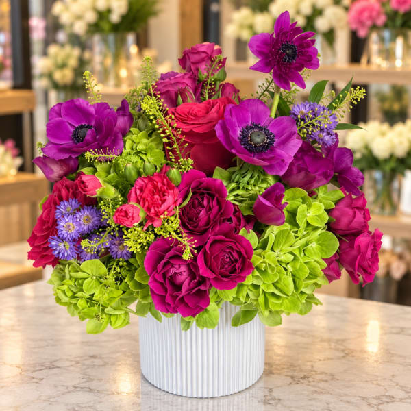 Bright magenta and purple bouquet in a white ribbed vase