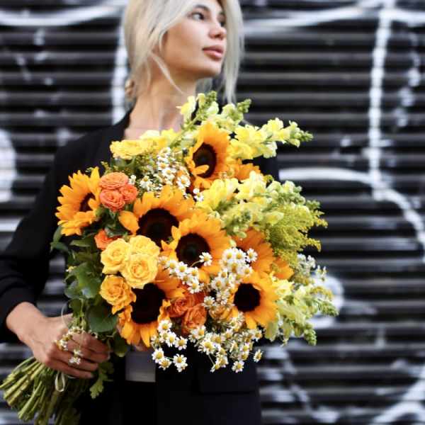Woman holding a large bouquet of sunflowers, roses, and small white daisies