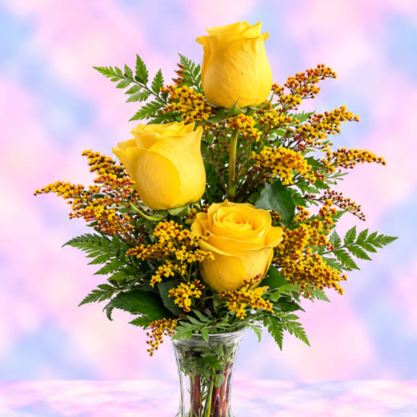 Yellow roses in a clear glass vase with small yellow filler flowers