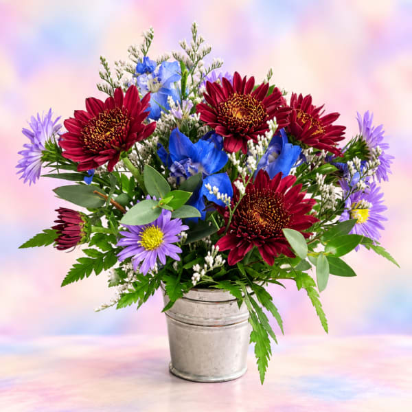 Mixed bouquet of red, blue, and purple flowers in a metal bucket
