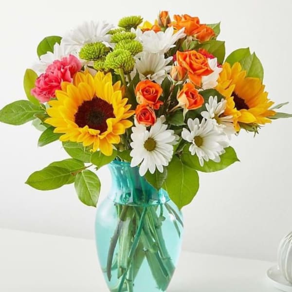 Mixed bouquet of sunflowers, daisies, roses, and carnations in a blue vase