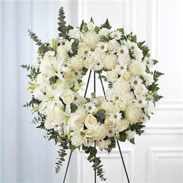 White funeral wreath on a black easel with lilies, roses, and daisies