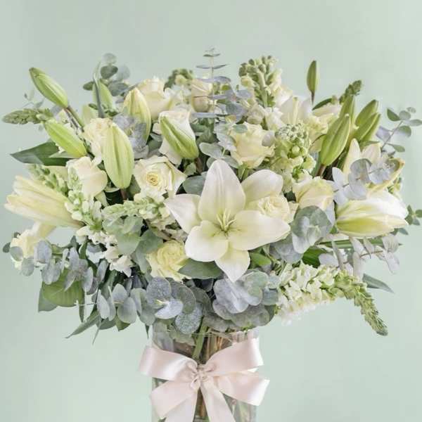 White lilies and roses in a glass vase with a pale ribbon