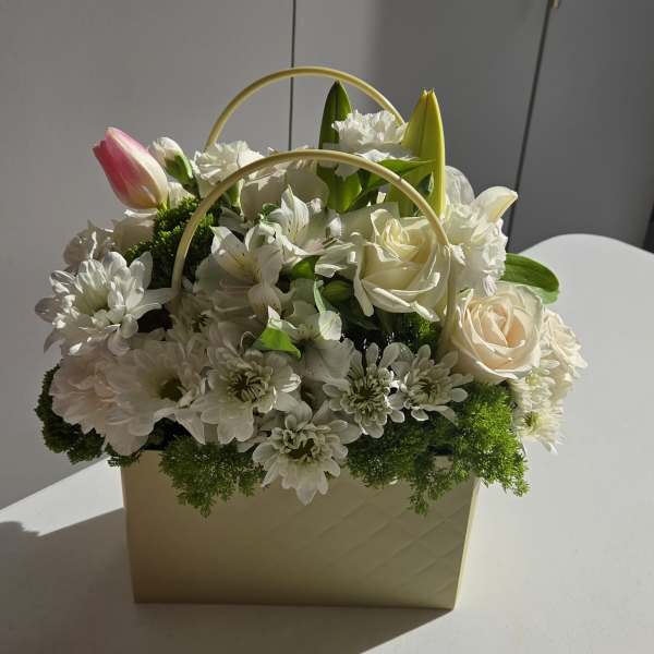 White floral arrangement in a cream handled box with pink tulip and roses