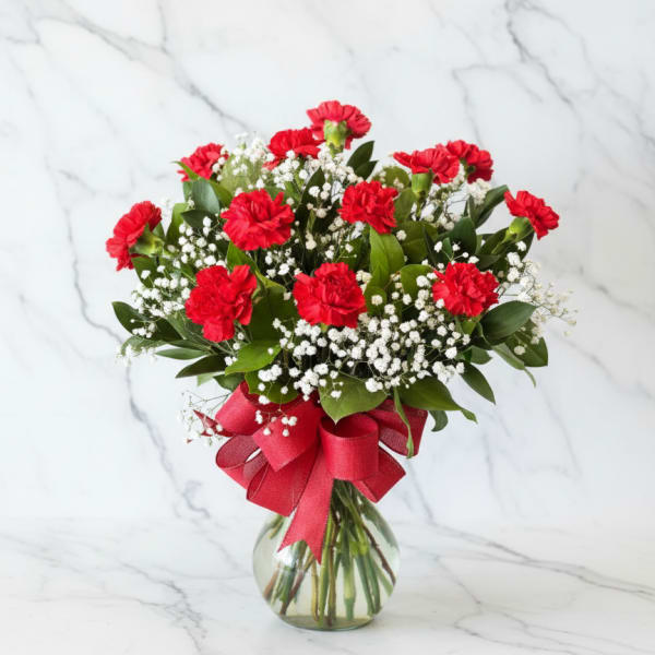 Red carnations and baby's breath in a glass vase with a red ribbon