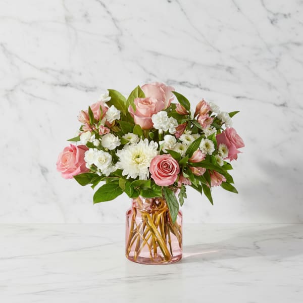 Pink roses and white flowers arranged in a pink glass vase