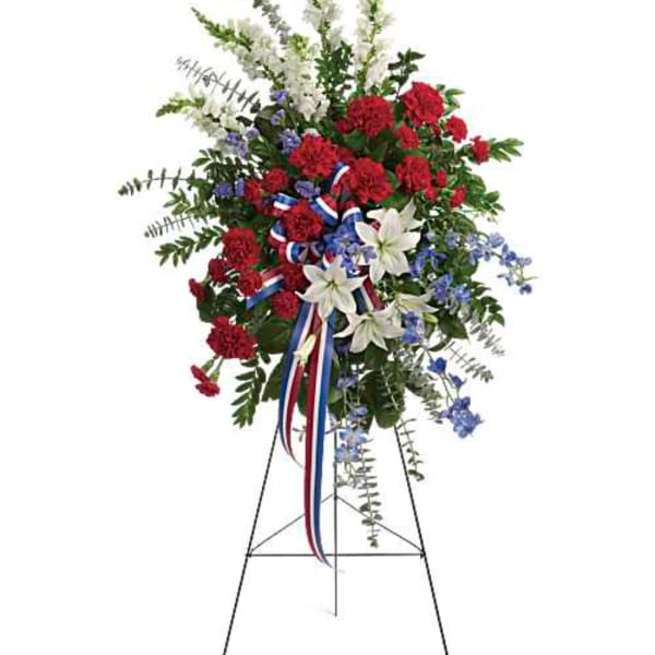 Standing floral spray with red carnations, white lilies, and blue flowers on an easel