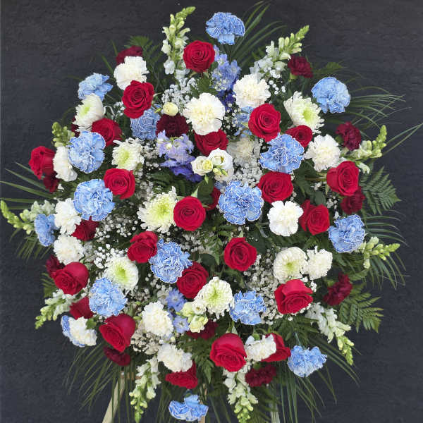 Large standing floral spray with red roses, blue carnations, and white blooms