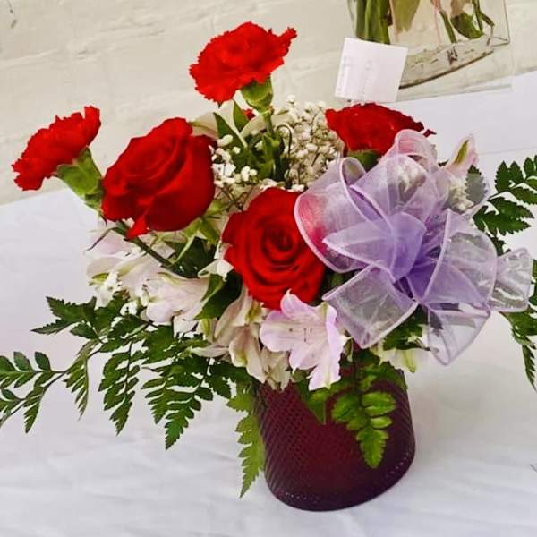Red roses and carnations in a purple vase with a lavender bow