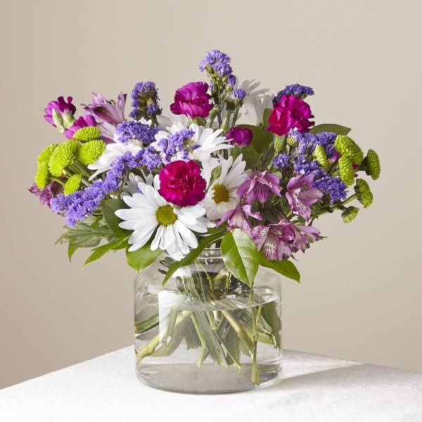 Mixed bouquet of daisies, carnations, and purple blooms in a glass vase