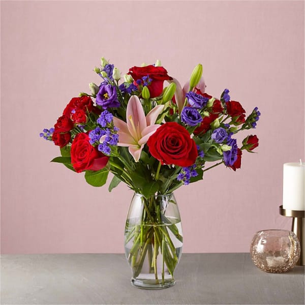 Bouquet of red roses, purple blooms, and a pink lily in a glass vase