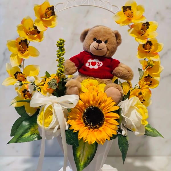 Teddy bear in a red shirt surrounded by yellow flowers and white roses