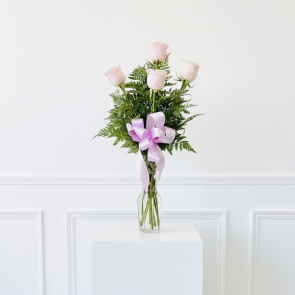 Five pale pink roses in a clear glass vase with a lavender ribbon