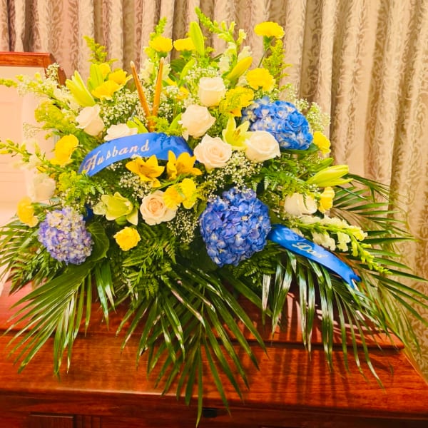 Large mixed flower arrangement with blue ribbons and a "Husband" sash