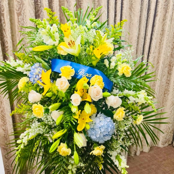 Large standing floral arrangement with yellow lilies, white roses, and blue hydrangea