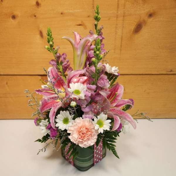 Pink lilies and daisies arranged in a glass vase with a ribbon